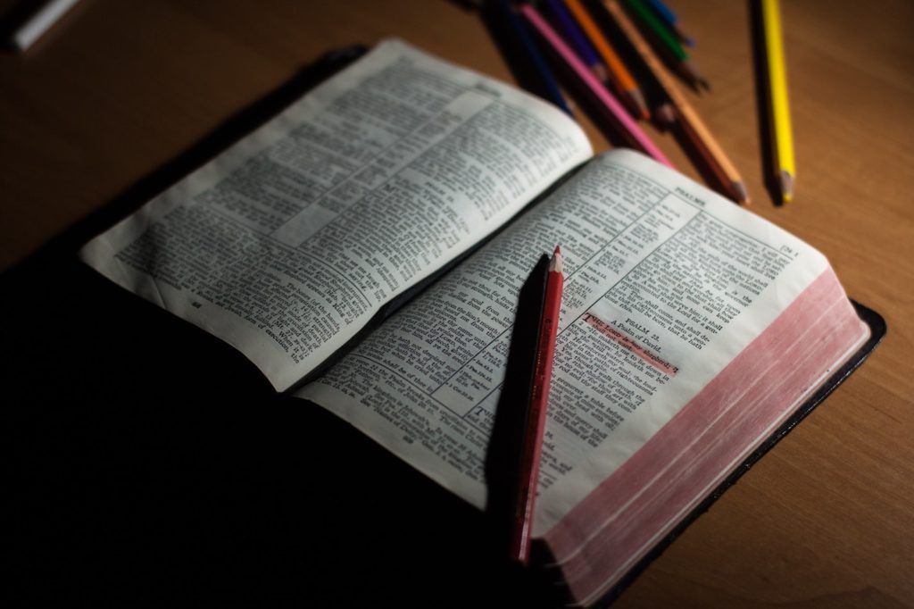 An open Bible with a red pencil next to it on a wooden surface, indicating the use of journaling for spiritual discovery.